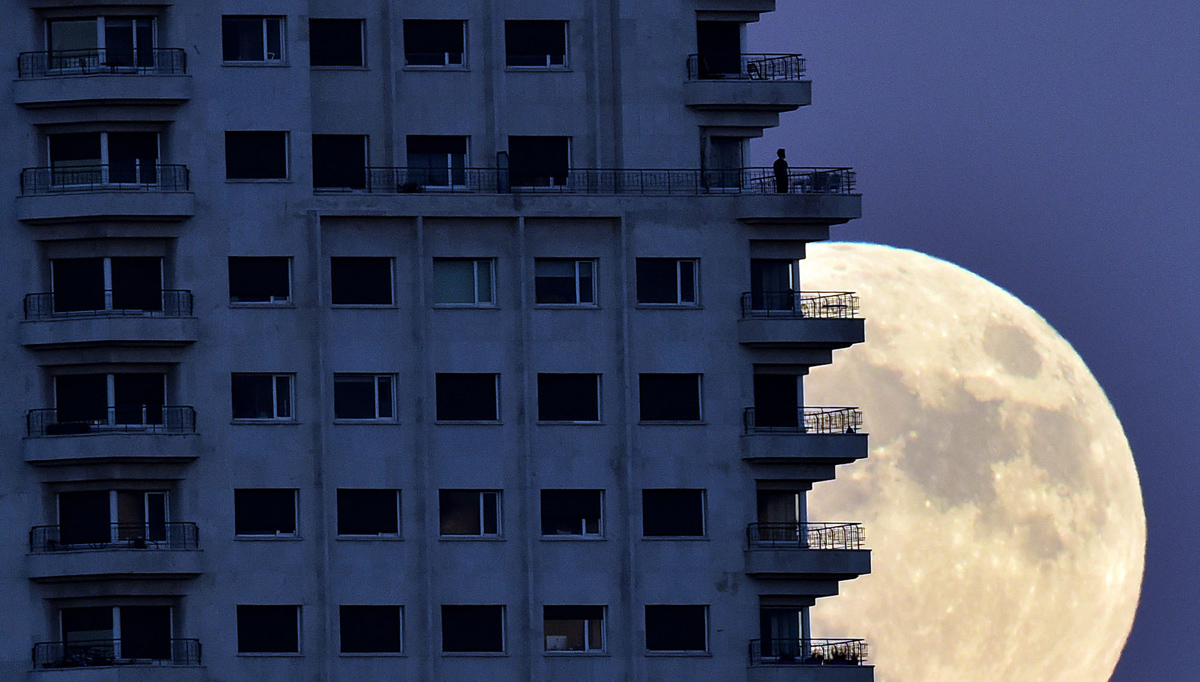 A man stands on a balcony of a building of Madrid as the moon rises in background, on November 13, 2016, on the eve of a "supermoon". On November 14, 2016, the moon will orbit closer to the earth than at any time since 1948, named a 'supermoon', it is defined by a Full or New moon coinciding with the moon's closest approach to the Earth. / AFP / GERARD JULIEN (Photo credit should read GERARD JULIEN/AFP/Getty Images)