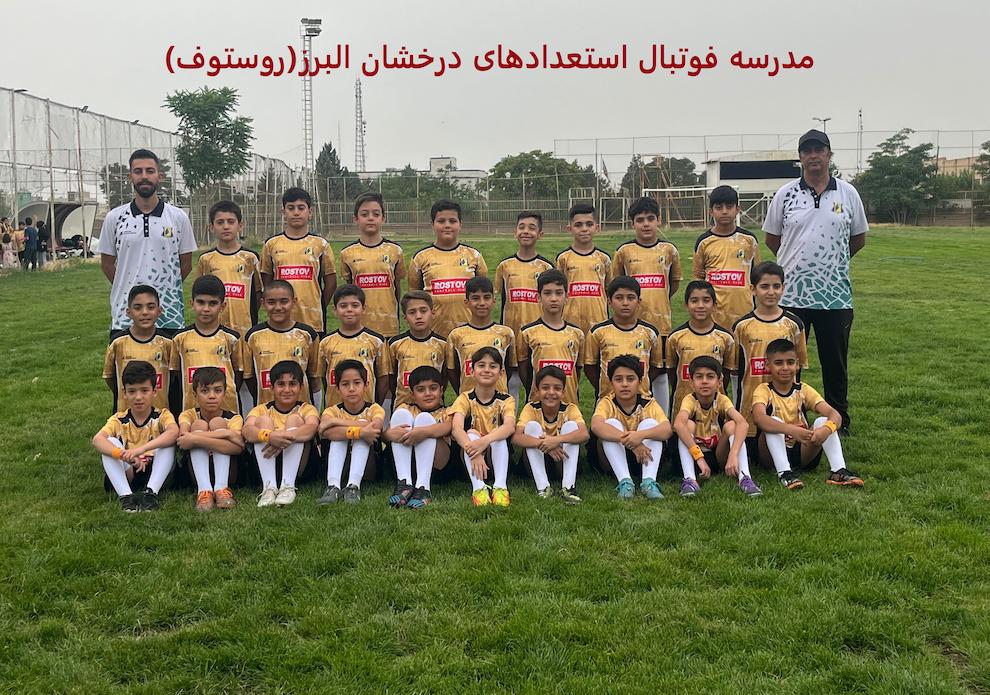 عکس تیمی فوتبالیستهای نوجوان با لباسهای طلایی مشکی در زمین چمن طبیعی با دو مربی خود با لباسهای سفید